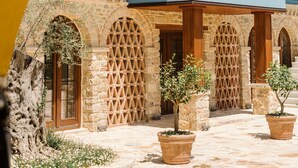 A courtyard with a blue building, stone arches, and potted plants. - Blerina's Village Project  (Kamëz)