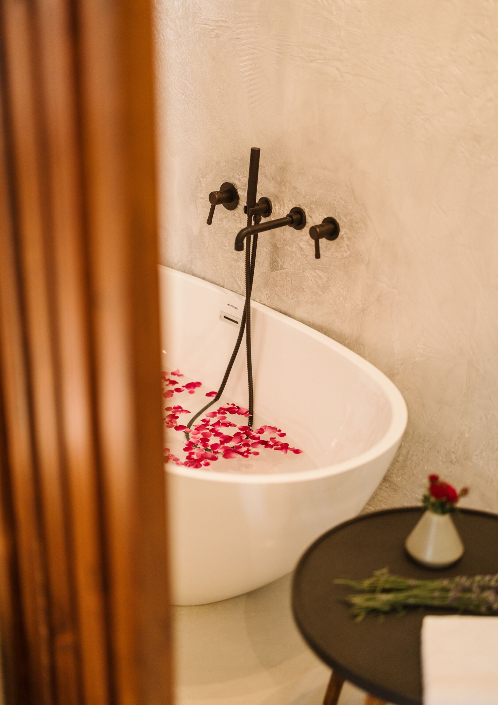Una vasca da bagno con petali di rosa, un asciugamano e un vaso con fiori su un tavolino.