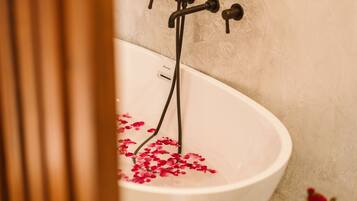 Una vasca da bagno con petali di rosa, un asciugamano e un vaso con fiori su un tavolino.