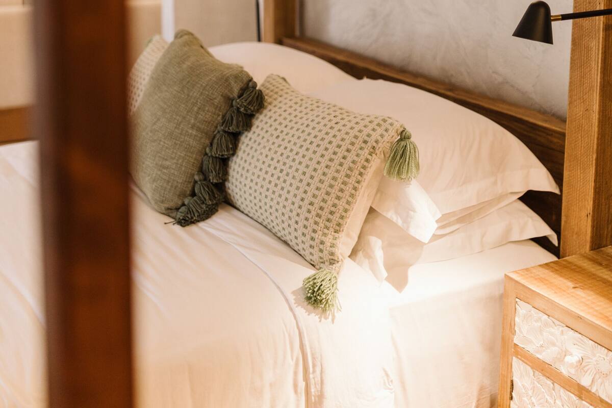 Una cama bien hecha con una colcha y almohadas estampadas, un cuadro de un árbol en la pared y un cabecero de madera.