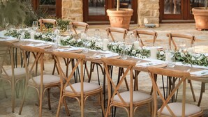 An outdoor dining area with stone tables, wooden chairs, and potted plants. - Blerina's Village Project  (Kamëz)