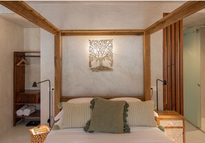 A bedroom with a wooden headboard, a wall-mounted tree decoration, a bed with pillows, a bedside table, a lamp, a shelf with towels, and a wardrobe. - Blerina's Village Project  (Kamëz)