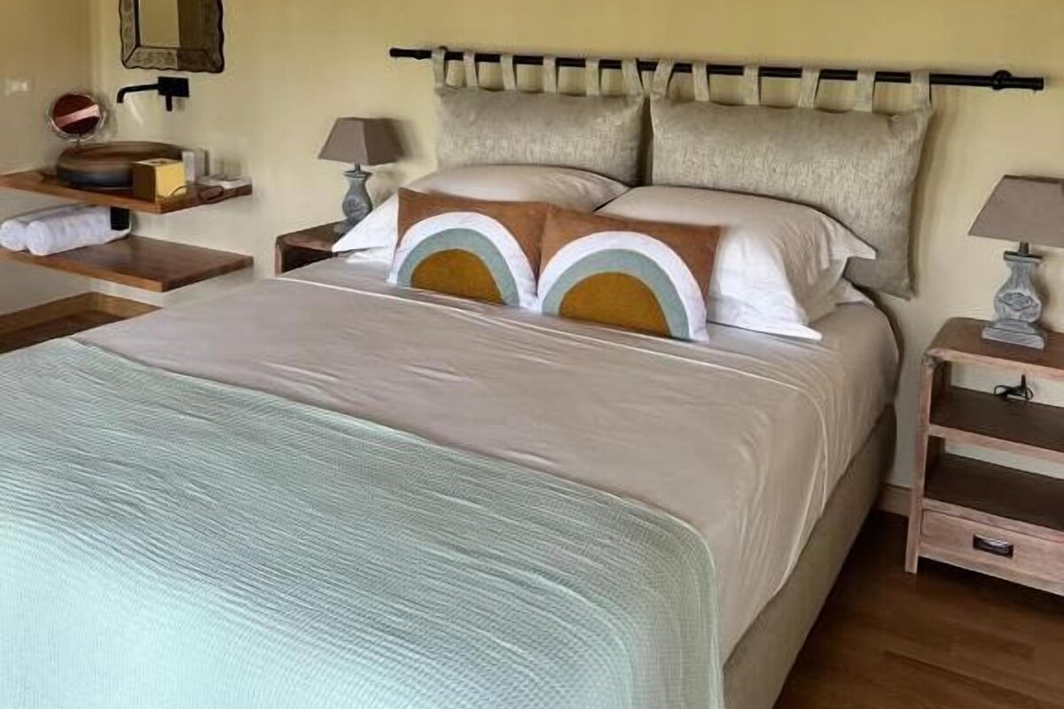 Un dormitorio con cama, mesitas de noche, un espejo y una viga de madera en el techo.