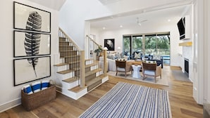 Amplia sala de estar con escalera, chimenea y grandes ventanales con vistas al exterior.