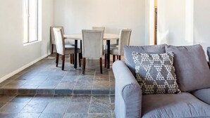 A spacious living room with a grey sofa, patterned throw pillow, and a dining area with a table and chairs.