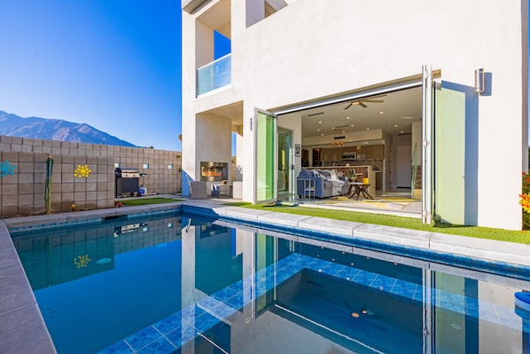 A modern house with a swimming pool, a patio, and a view of mountains.