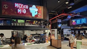 Un restaurante con un letrero de neón que dice "Mexico MIO" y una zona de mostrador donde el personal prepara alimentos.