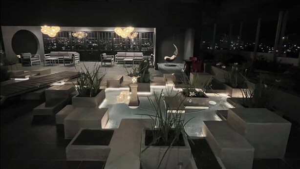 Un área de descanso al aire libre con asientos, jardineras y vistas de la ciudad de noche.