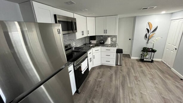 Una cocina moderna con electrodomésticos de acero inoxidable, armarios blancos y piso de madera gris.