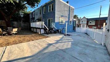A residential building with a front yard, a staircase leading to the entrance, and a fenced backyard.