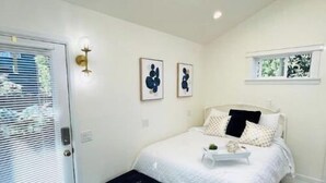 A bedroom with a bed, a black bench, patterned rugs, and wall art. - Light, bright & clean, studio guest suite with private entrance and hot tub! (Redmond)
