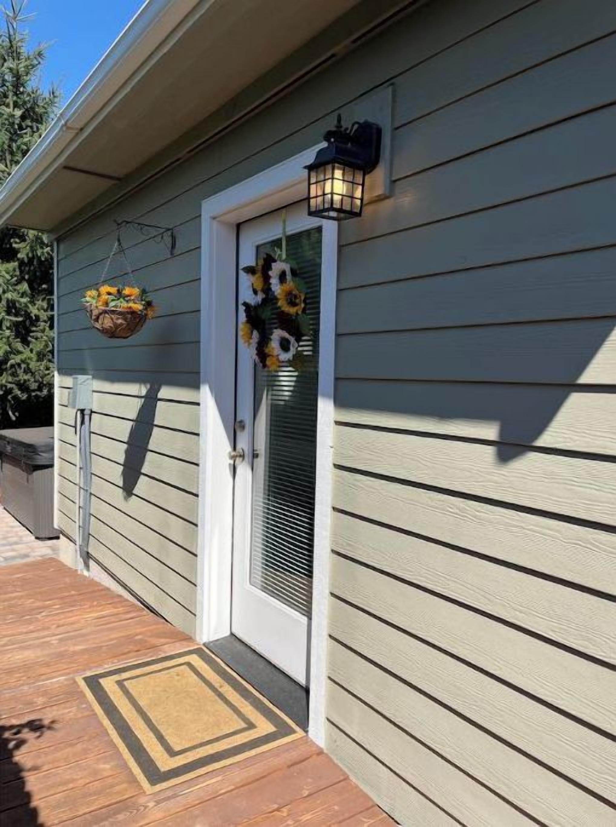 A house with a wooden deck, a door with a decorative wreath, and a wall-mounted lantern.
