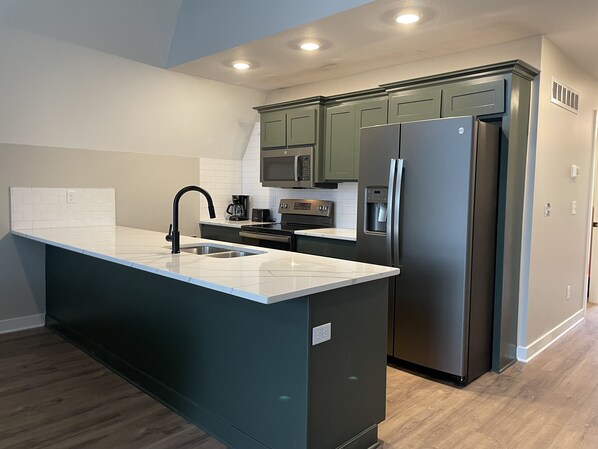 A modern kitchen with a central island, stainless steel appliances, and green cabinetry. - Hilltop Hideaway at Station 46 (Gravois Mills)