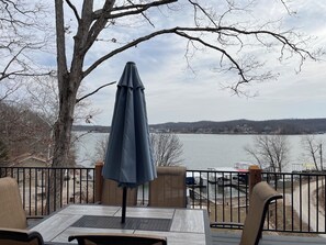 A deck with a table and chairs, overlooking a lake with a view of buildings and hills in the distance. - Hilltop Hideaway at Station 46 (Gravois Mills)