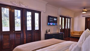 Een hotelkamer met een groot bed, een aan de muur bevestigde televisie, een bureau met een lamp en uitzicht naar buiten door de ramen.