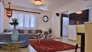 Een moderne woonkamer met een bank, een glazen salontafel, een rood tapijt met patroon en een decoratieve vaas.