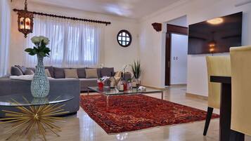 A modern living room with a sofa, a glass coffee table, a red patterned rug, and a decorative vase.