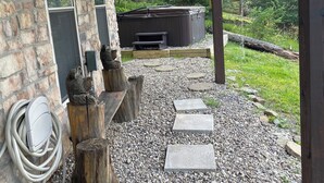 A stone building with a covered patio area, a hot tub, and a gravel pathway leading to a wooden deck.
