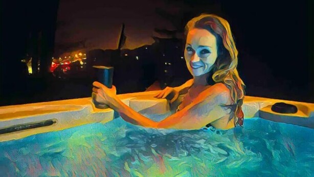 A person relaxing in a hot tub at night with city lights in the background.