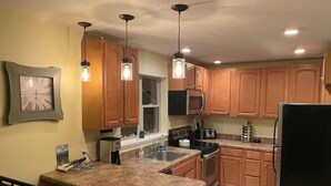 A kitchen with wooden cabinets, a granite countertop, a microwave, a refrigerator, and pendant lighting.