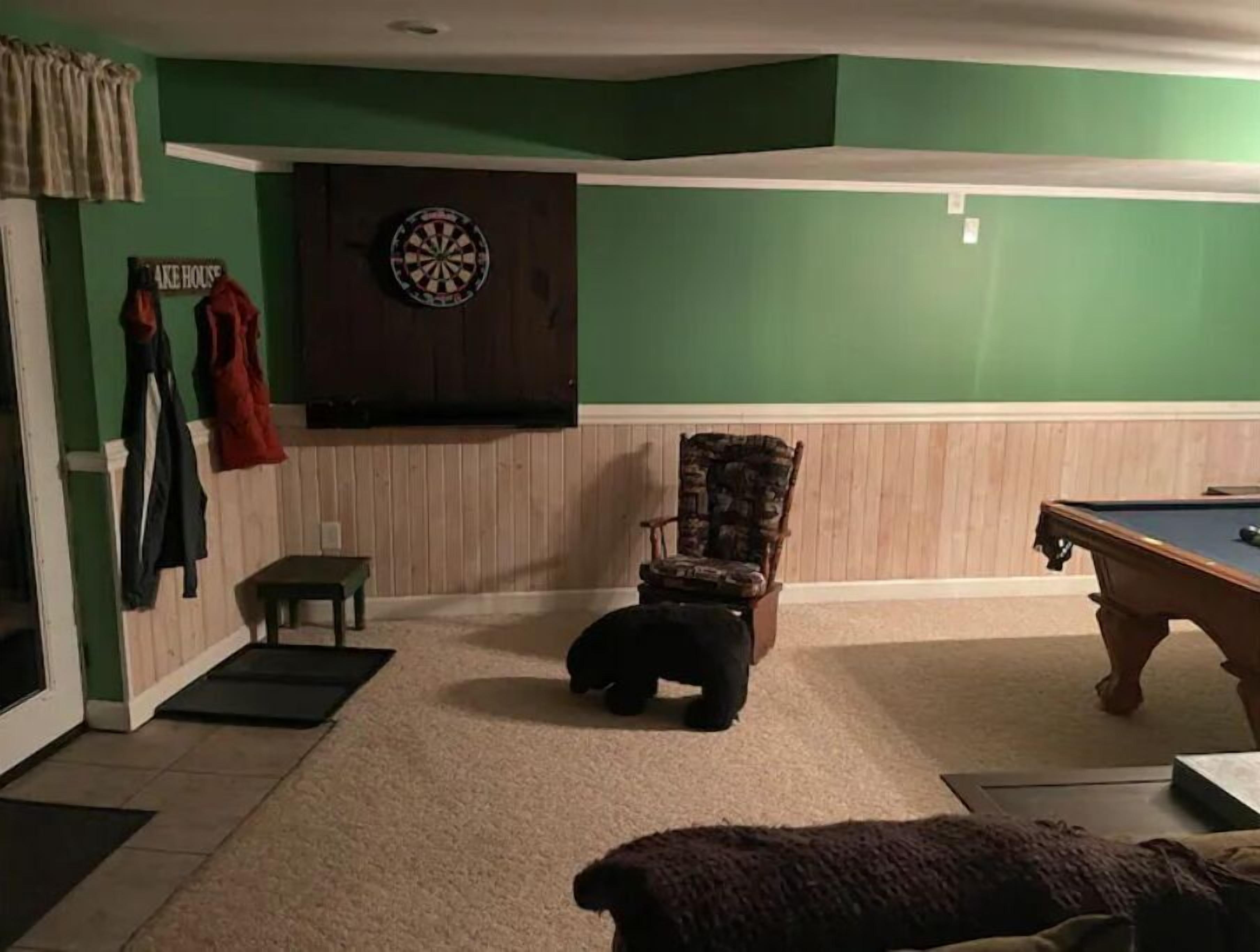 A room with a dartboard, a pool table, a chair, and a small table.