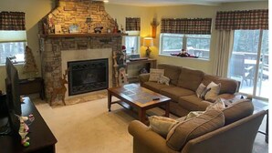 A cozy living room with a stone fireplace, a sofa, a coffee table, and plaid curtains.