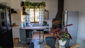 Et moderne køkken med en central ø, barstole, et køleskab og diverse planter.