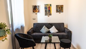 En moderne stue med en grå sofa, to sorte lænestole, et glasbord og tre kunstværker på væggen.