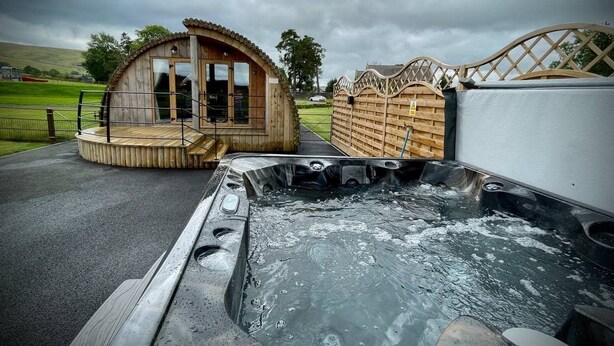 A hot tub with a wooden deck, a wooden cabin, and a wooden fence.
