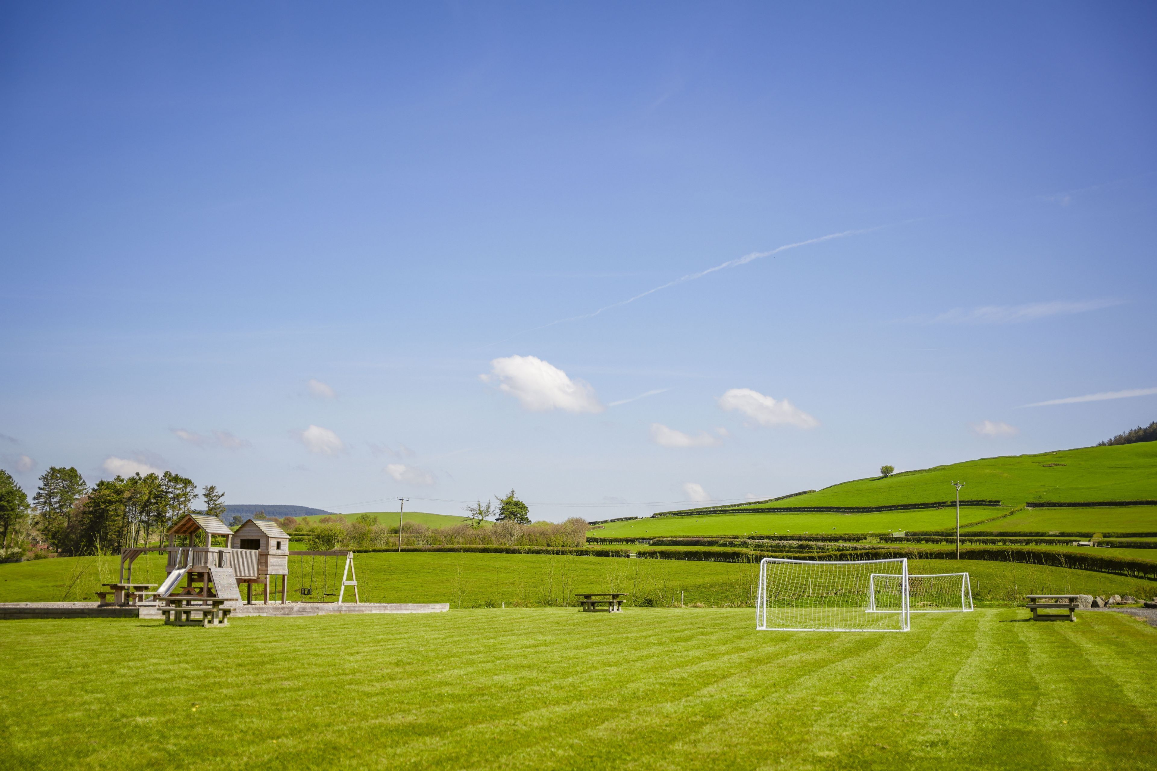 Un terrain de football avec des buts, des tables de pique-nique et une structure de jeux en bois.