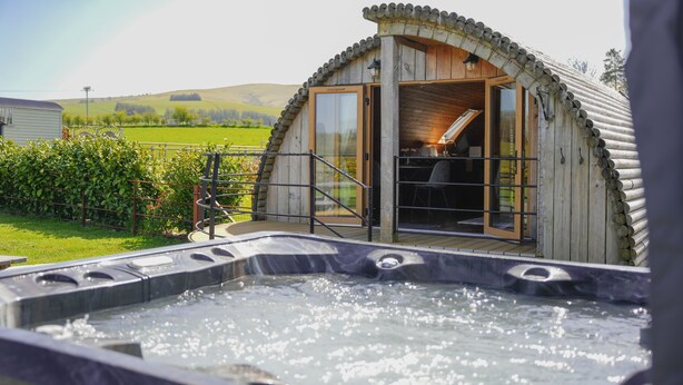 Ein rustikales Holzhaus mit Whirlpool, einer Holzdiele und Blick auf die Landschaft.
