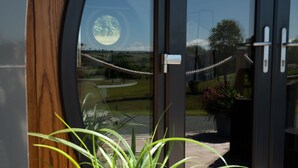 A view through a glass door with a rope barrier, a wooden deck, and a potted plant. - Bedwen -  Glamping pod with Hot Tub sleeping 2 guests (Welshpool)