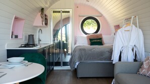 A cozy bedroom with a bed, a window, a sink, and a small table with chairs. - Celyn -  Glamping Pod with hot Tub Sleeping 2 People (Welshpool)