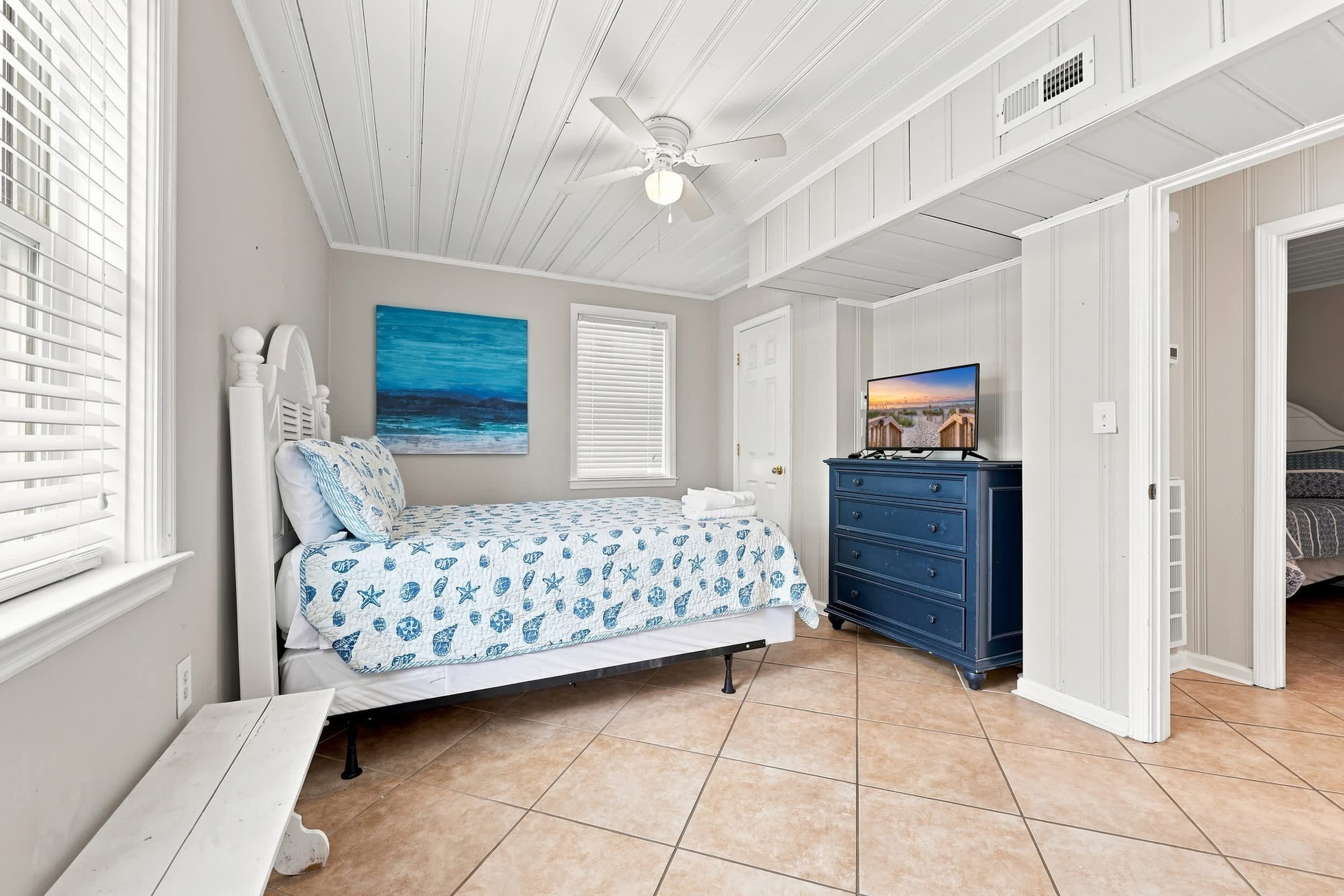 A bedroom with a bed, a dresser, a ceiling fan, and a painting on the wall.