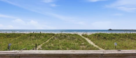 A wooden deck with a view of the beach and a pier in the distance.