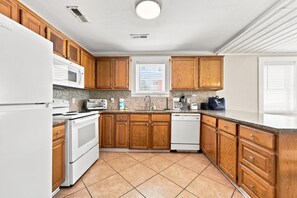 A kitchen with wooden cabinets, a white refrigerator, a stove, a microwave, a dishwasher, and a window with blinds. - Hazels Castle Huge 2 in 1 Oceanfront House near  Pier (North Myrtle Beach)