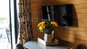 Ein Holzinterieur mit einem runden Tisch, zwei Stühlen, einem an der Wand montierten Fernseher und einem Fenster mit Vorhängen.