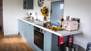 A kitchen with a central island, a sink, a stove, and a clock on the wall. - Cwm Heulog -  Cabin with Hot Tub Sleeping 4, Pet Friendly (Knighton)