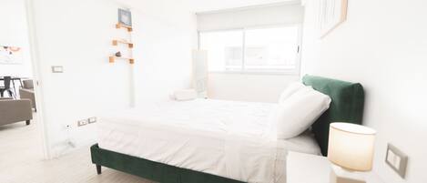 Una habitación de hotel moderna con una cama tapizada en verde, una lámpara de noche y una ventana con vistas.