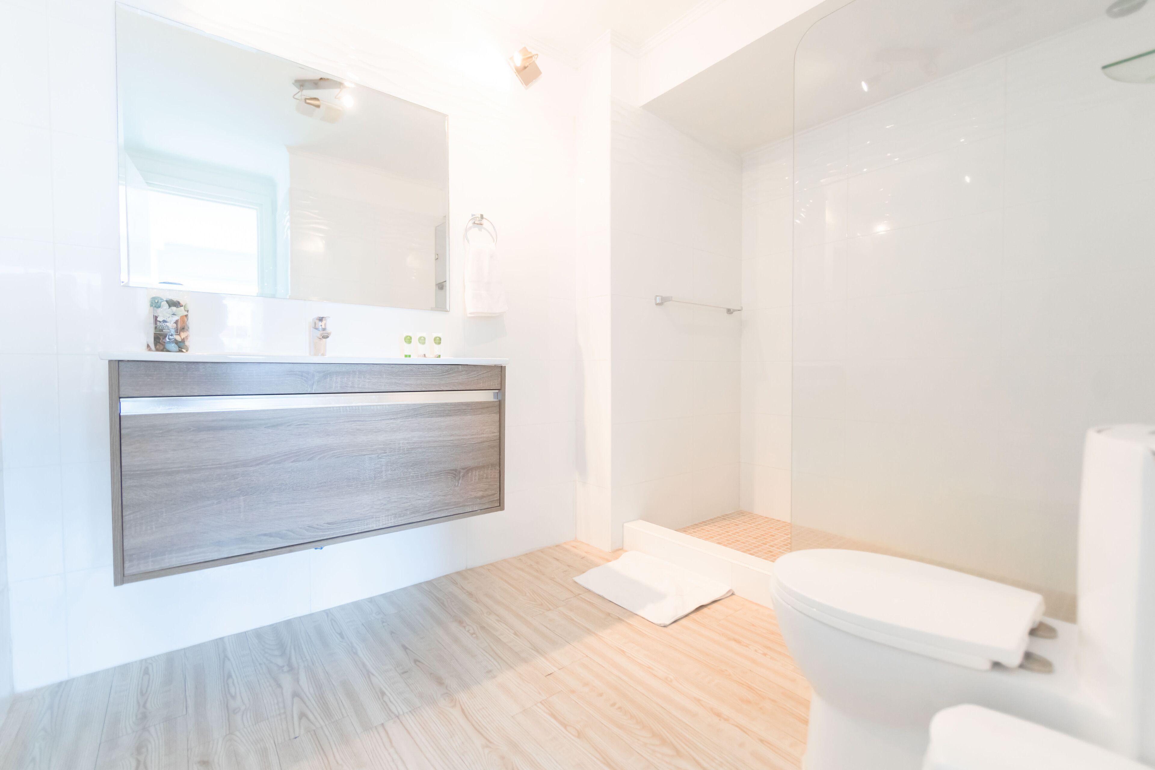 A modern bathroom with a wooden vanity, a large mirror, and a shower area.