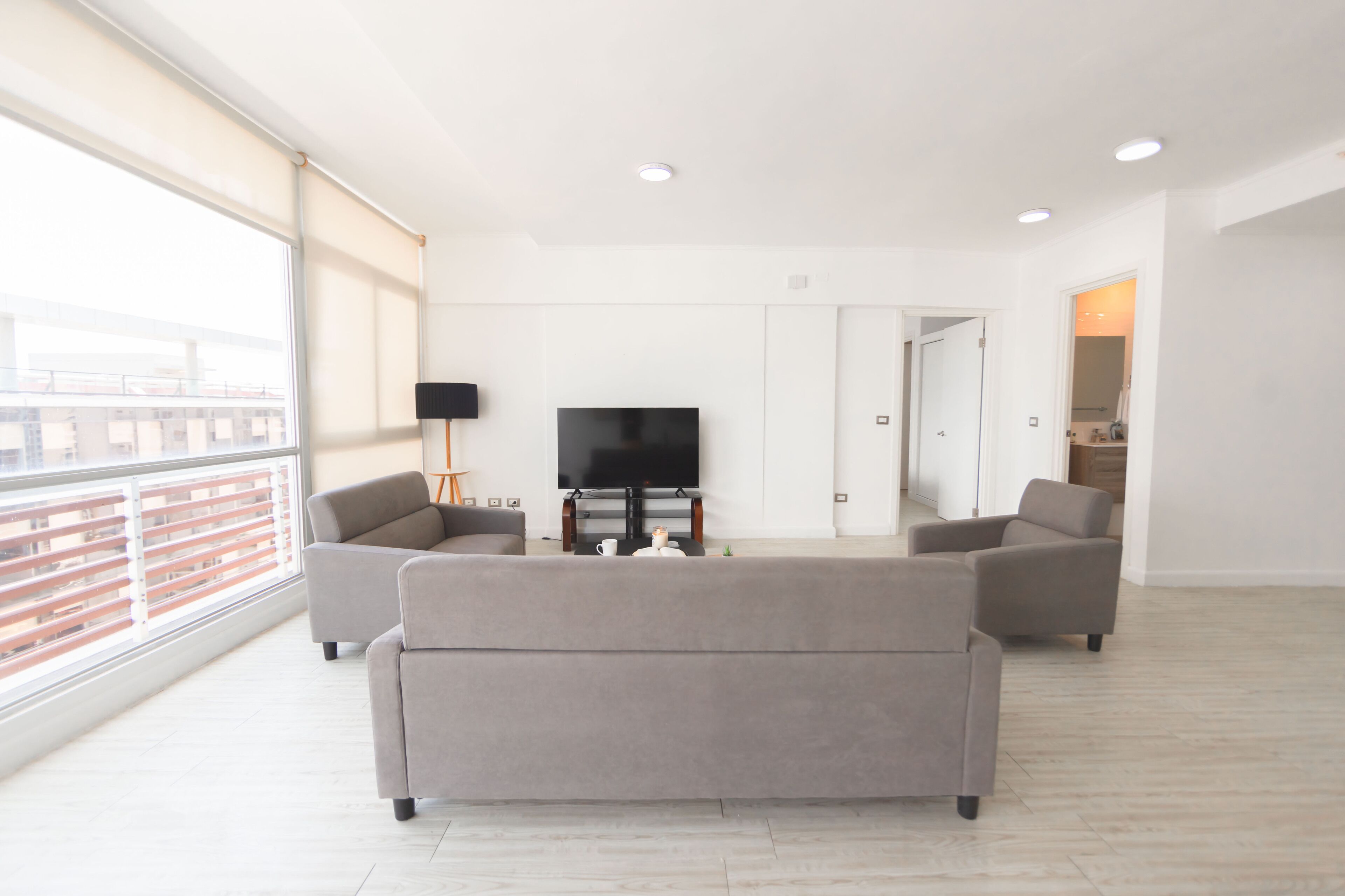 A spacious living room with a large window, a flat-screen TV, and two grey sofas.