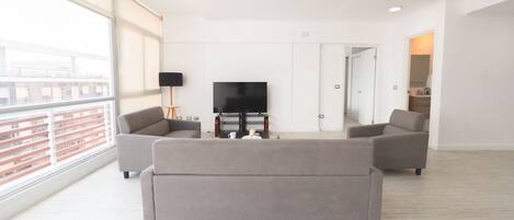 A spacious living room with a large window, a flat-screen TV, and two grey sofas.