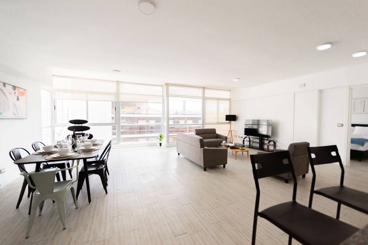 A spacious living area with a dining table set for four, a sofa, and a TV.