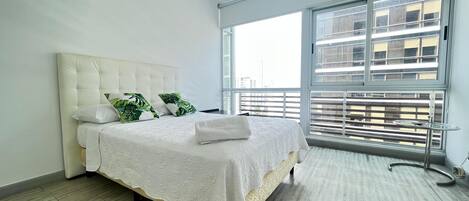 Un dormitorio con una cama grande, una ventana con persianas y vistas a edificios.