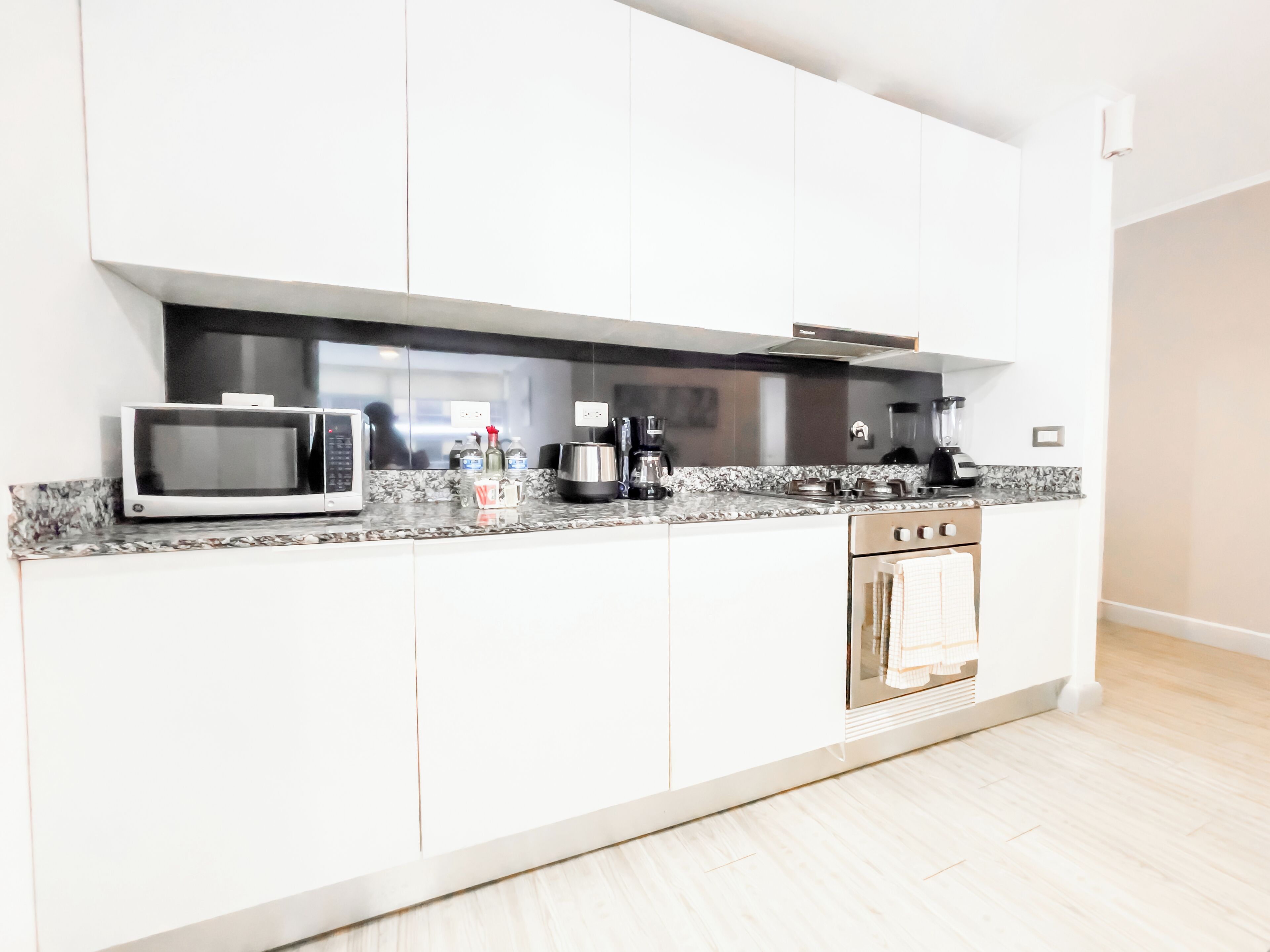 A modern kitchen with white cabinets, a microwave, a coffee maker, and a built-in oven.