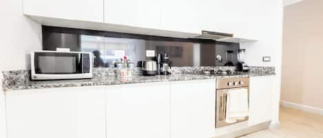 Una cocina moderna con armarios blancos, microondas, cafetera y horno empotrado.