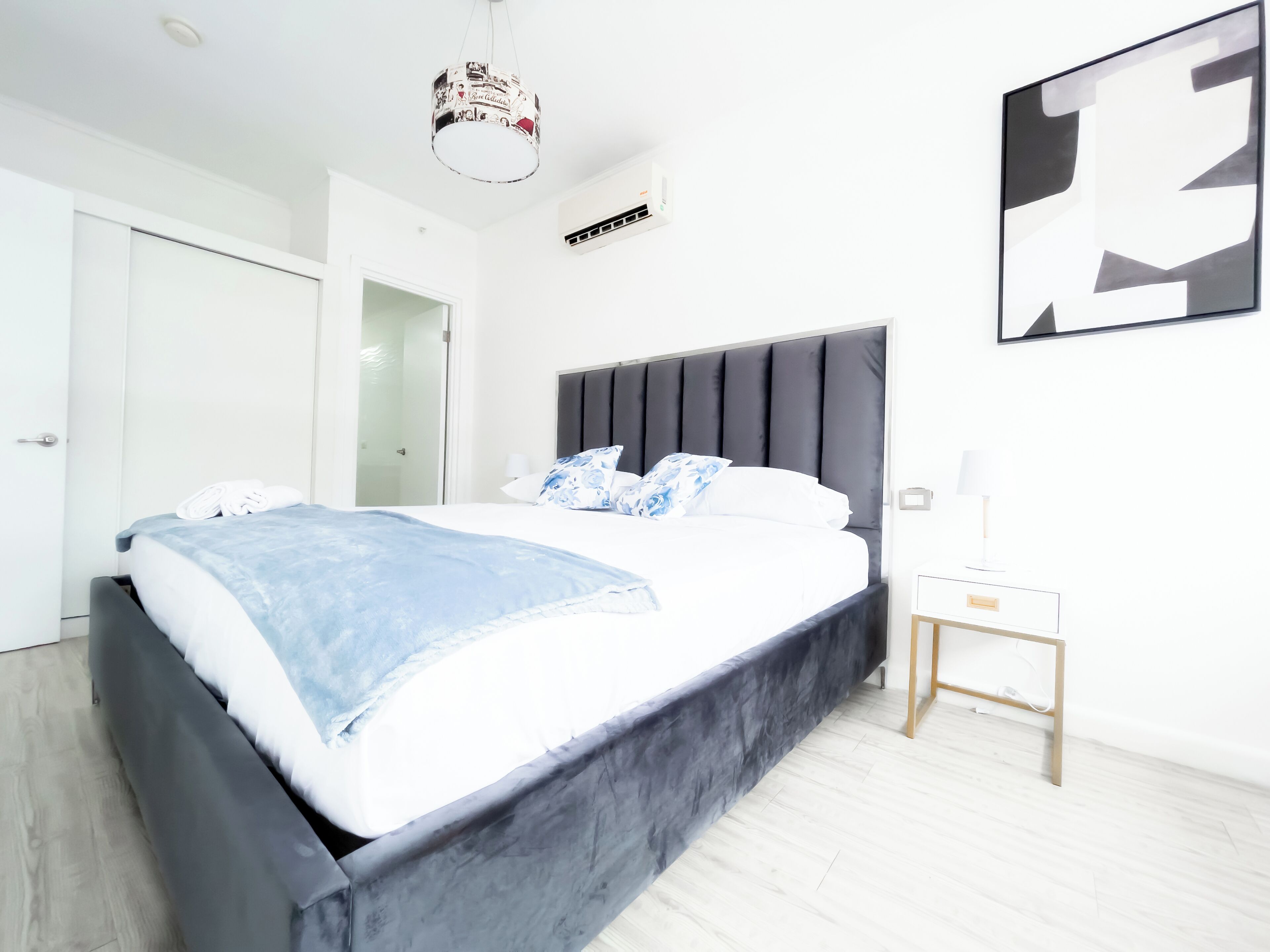 Un dormitorio moderno con una cama grande, una mesita de noche, una lámpara de techo y un aire acondicionado instalado en la pared.