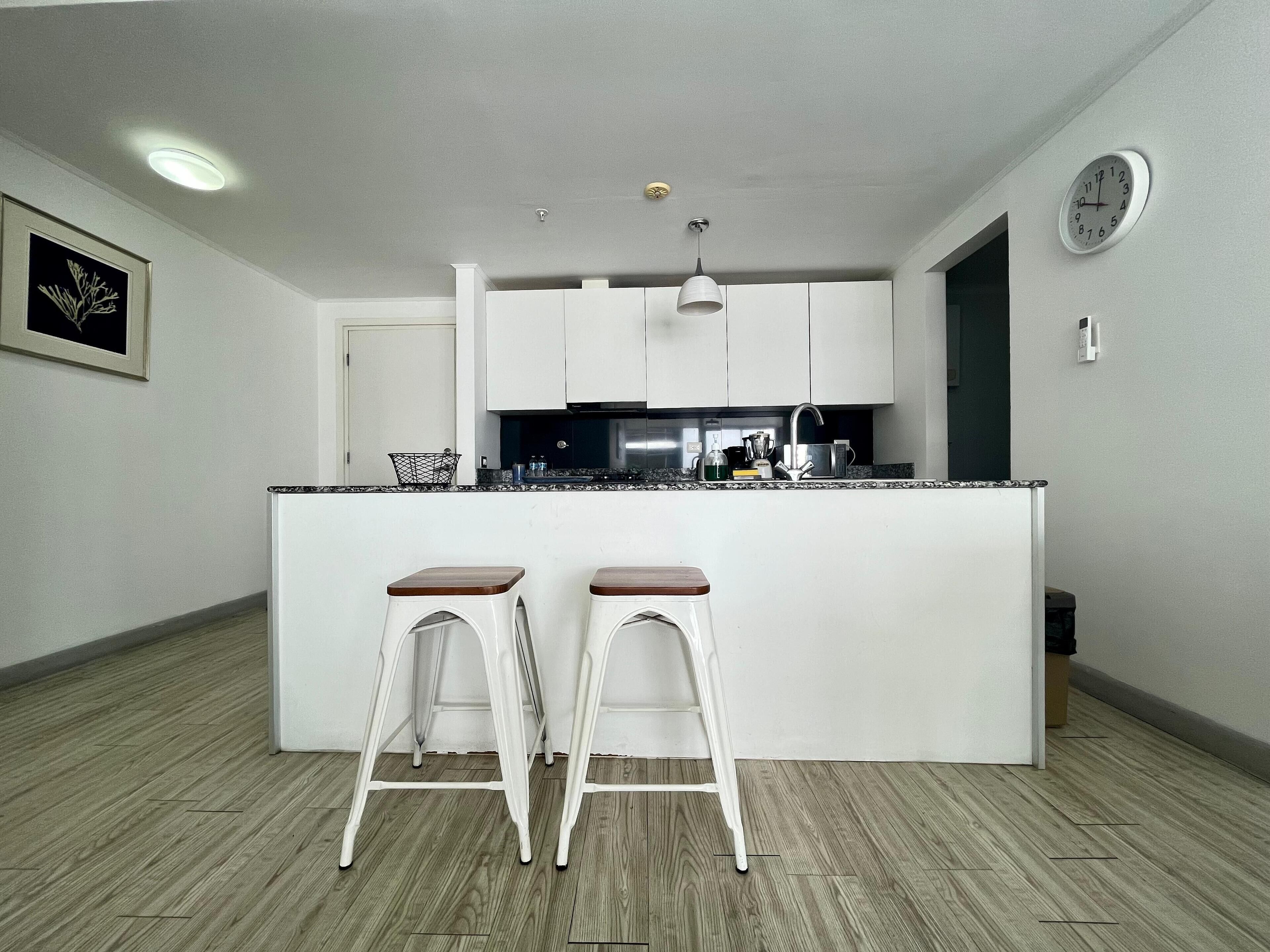 A modern kitchen with white cabinets, a black countertop, and two white stools.