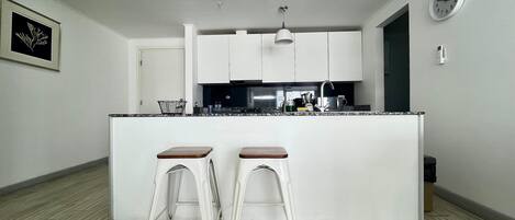 A modern kitchen with white cabinets, a black countertop, and two white stools.