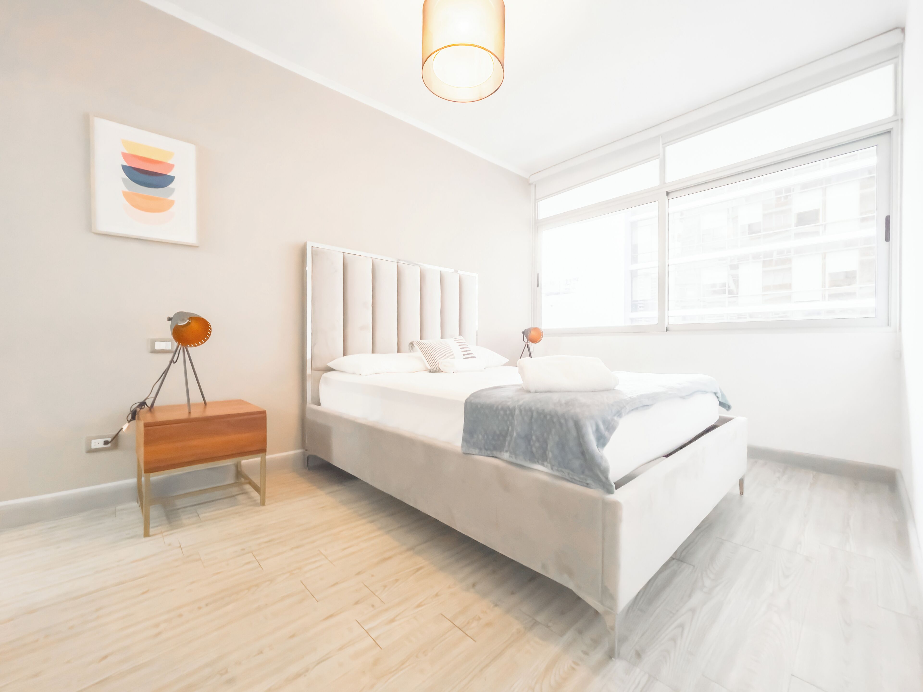 A modern bedroom with a bed, bedside table, lamp, and artwork on the wall.